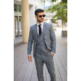 Man wearing a gray suit and sunglasses on a city street.