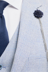 Man wearing a light gray suit with a navy tie and flower pin on a white background