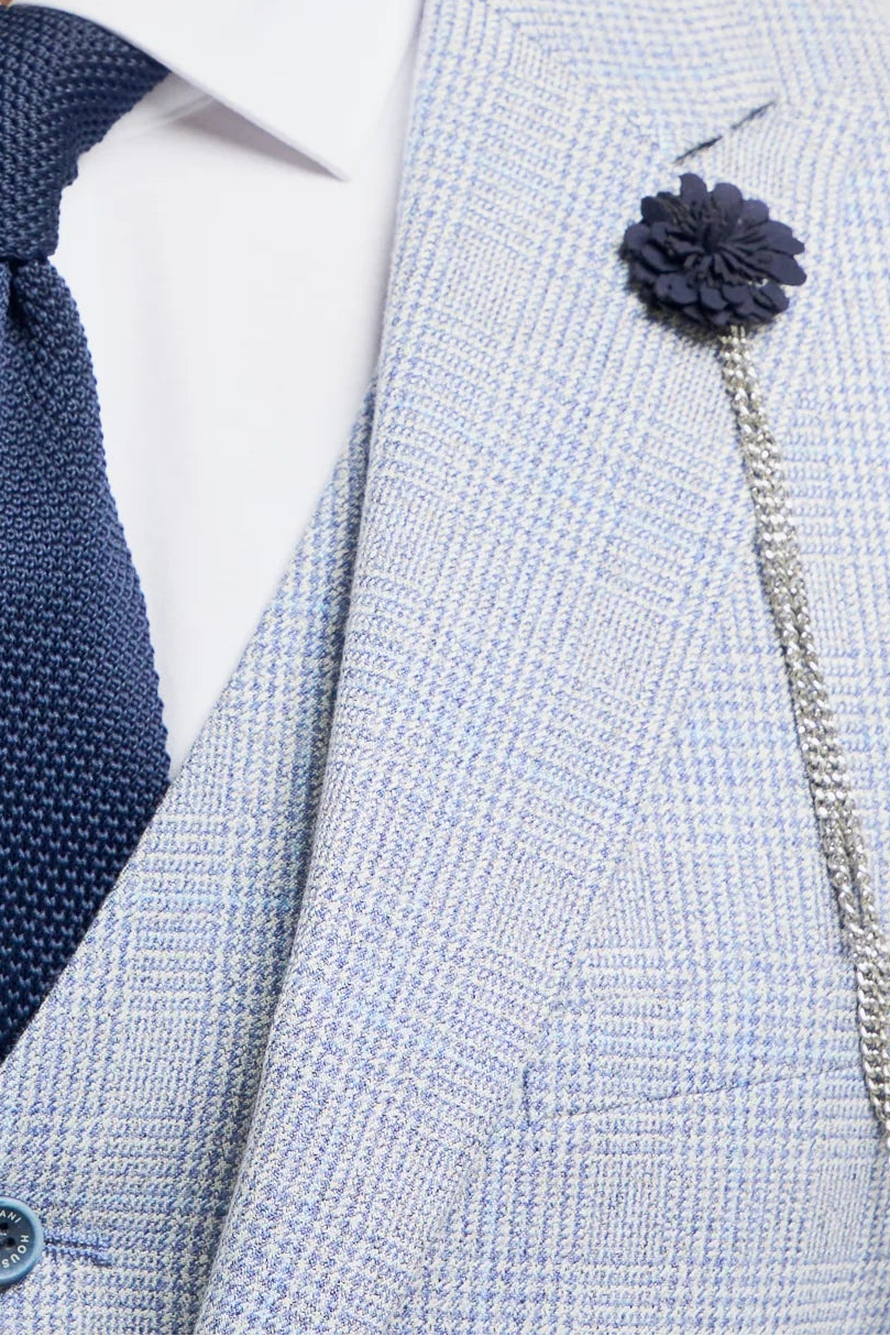 Man wearing a light gray suit with a navy tie and flower pin on a white background