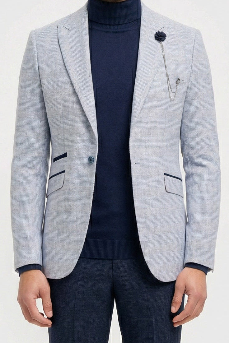 Man wearing a light gray blazer, navy turtleneck, and dark pants on a white background