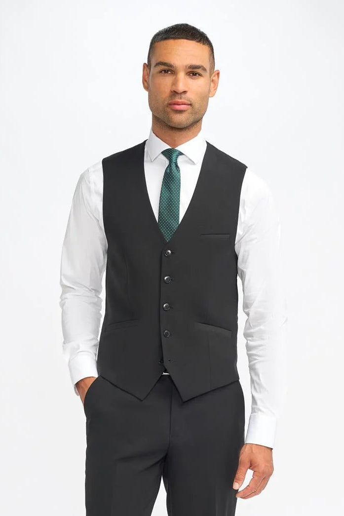 Man wearing a black suit vest over a white shirt with a green tie on a white background